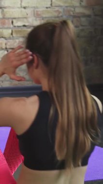 Canlı bir fitness stüdyosunda, kendini işine adamış bir antrenör müşterisine mekik çekmede yardımcı olur, takım çalışmasını ve kararlılığını gösterir. Renkli spor kıyafetleri ve dokuma hasırlarıyla vurgulanan enerjik atmosfer, onların kararlılıklarını vurguluyor.