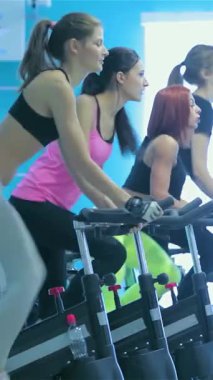 Kararlı dört genç kadın, parlak ve modern bir spor salonunda hareketsiz bisiklete binerek güç ve motivasyon yayıyorlar. Canlı mavi duvarlar ve akan doğal ışık ile vurgulanan bu canlı atmosfer, onların coşkulu ruhlarını güçlendirir.