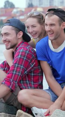 Üç neşeli arkadaş yazın sıcağında güneşlenirken, bir kız neşe içinde neşe içinde arkadaşlarına sarılıyor. Nehir kenarında parıldayan gülücüklerini paylaşıyorlar. Bu canlı sahne, dostluk ve kaygısız maceraların ruhunu yansıtıyor.