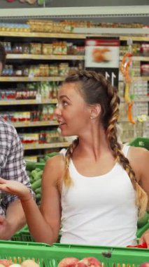 Neşeli genç bir çift canlı portakalları renkli taze sebzeler arasında inceleyerek keyifli bir alışveriş anını paylaşıyor. Işıltılı gülümsemeleri ve şakaları sağlıklı yiyecekleri birlikte seçmenin, aşkı somutlaştırmanın ve