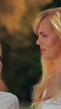 Güneşli bir parkta, neşeli bir anne ve genç kızı içten bir anı paylaşıyor, parlak gülümsemelerle alınlarına nazikçe dokunuyorlar. Bağlantıları canlı yeşillik boyunca parlıyor, aile bağlarının sıcaklığını ve sevgisini somutlaştırıyor.