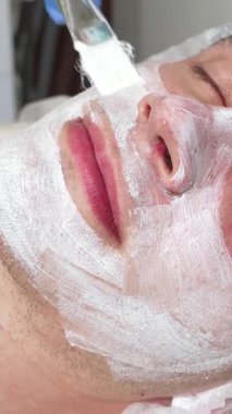 Yakışıklı bir adam huzur içinde uzanıyor, gözleri kapalı, yetenekli bir güzellik uzmanı nazikçe yüz maskesi takıyor, tenini rahatlatıcı gıdayla kaplıyor. Yumuşak ışıklandırma ve barışçıl dekorla spa 'nın rahatlatıcı atmosferi,