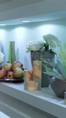 Çok güzel sergilenen raflarda şık vazolarda sersemleten beyaz çiçekler, canlı narlar ve yumuşak mumlar sergileniyor. Huzurlu ve davetkar bir atmosfer yaratıyorlar. Bu hoş düzenleme doğanın güzelliğini zarif bir dekorla harmanlıyor, mükemmel.