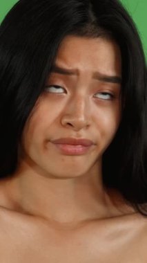Büyüleyici, uzun, ipeksi saçları olan genç Asyalı bir kadın canlı, yeşil bir krom arka plana karşı duruyor. Şüpheci ifadesi, canlı bir şekilde hayal kırıklığını gösteriyor. Kusursuz cildi ve çarpıcı özellikleri izleyicileri duygularıyla empati kurmaya davet ediyor.