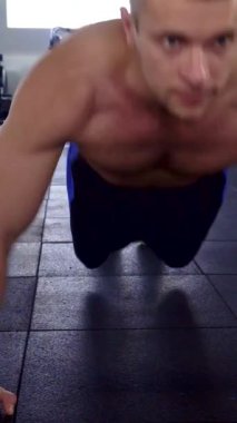 Kararlı bir Kafkasyalı, parlak, karanlık bir spor salonunda şınav çeker. Heykel şeklini ve güçlü formunu sergiler. Atmosfer enerjiyle doludur. Dikkatle odaklanır. Vücutta terler parıldar ve özünü somutlaştırır.