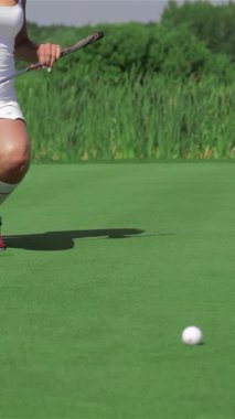 Beyaz atletik bir kadın, topu deliğe sokmaya hazırlanırken yoğun bir şekilde odaklanmış canlı bir golf sahasında zarifçe diz çöker. Şık kırmızı ayakkabıları ve kararlı duruşu, güneşli bir günün heyecanını somutlaştıran kendine güven ve beceri saçıyor.