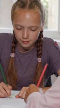 Saçları örgülü kararlı bir kız öğrenci renkli sanat projesiyle meşgul ve ilgili öğretmeninden sıcak bir teşvik alıyor. Bu canlı sınıf sahnesi yaratıcılığı yansıtıyor ve öğrenci ile öğrenci arasındaki bağın altını çiziyor.