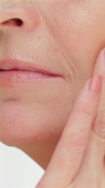 Zarif, yaşlı bir kadın zarif, pırıl pırıl tenine dokunur ve el değmemiş beyaz bir zemine vurgu yapar. Bu samimi an, özgüvenin ve özgüvenin özünü yakalar, izleyicileri kendi kutlamalarına davet eder.