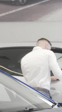 Şık bir işadamı, göz kamaştırıcı lüks araçlarla çevrili şık, çağdaş bir bayide çarpıcı mavi bir otomobili inceliyor. Bu canlı sahne araba alışverişinin heyecanını özetliyor. Şıklığı ve heyecanı vurguluyor.