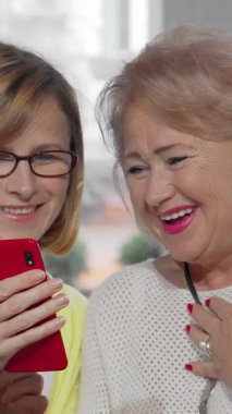 Olgun bir kadın, neşeli, kıdemli annesiyle canlı kırmızı akıllı telefonunda zevkli bir keşfi paylaşırken heyecanla ışıldıyor. İkisi de kahkahalarla kaplanıyor. Samimi bir kafede geçen bu iç açıcı sahne, sıcaklığı güzel bir şekilde gözler önüne seriyor.