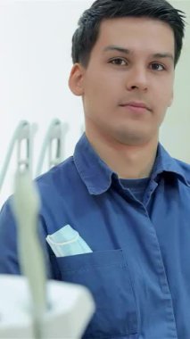 Gıcır gıcır mavi üniformalı arkadaş canlısı bir dişçi parlak bir gülümseme sergiliyor ve gösterişli, modern bir diş muayenehanesinde onay veriyor. Teknoloji harikası ekipmanlar ve temiz bir çevreyle dolu davetkar atmosfer, istisnai durumdaki hastaları