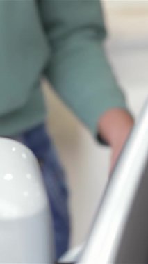 Tarz sahibi genç bir kadın danışman modern bir sergi salonunda gösterişli, parlak bir arabanın yanında duran kendine güvenen bir gülümseme ile saçını ve makyajını düzeltir. Bu canlı sahne profesyonelliği ve çekiciliği yansıtıyor, otomotiv satışlarındaki uzmanlığını vurguluyor ve