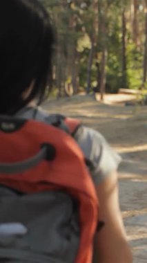 Neşeli bir esmer yürüyüşçü arkasını döner ve güneşin ıslattığı orman yolunda giderken ışıl ışıl gülüşünü gösterir. Modayı takip eden sırt çantası ve günlük kıyafetleri yemyeşil ile uyumlu, macera duygusunu ve keşfin heyecanını çağrıştırıyor.