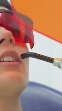 Parlak, klinik bir ortamda, koruyucu gözlüklerle süslenmiş yetenekli bir dişçi hastaların dişlerine ultraviyole bir mühür takarak birinci sınıf diş bakımı sağlar. Huzurlu atmosfer ve gelişmiş diş aletleri