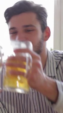 Kahkahalarla dolu canlı bir barda, üç neşeli arkadaş, açık ve koyu saçlı iki adam, buzlu bira bardaklarını neşeyle tokuşturarak arkadaşlığı ve güzel zamanları kutluyorlar. Bar ışıklarının sıcacık parıltısı festival atmosferini güçlendiriyor.