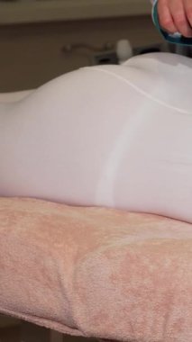 Keyifli genç bir kadın pelüş bir tedavi masasında cildini canlandıran LPG masajından zevk alıyor. Sahne huzur saçıyor, neşeli gülüşünü sergiliyor yetenekli bir güzellik uzmanının ustalıkla gelişmiş ekipmanları kullanması gibi.