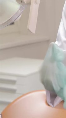 Kendini işine adamış bir erkek dişçiye yakın plan, el değmemiş beyaz bir tıbbi elbise giymiş, modern bir diş kliniğinde titizlikle steril eldiven takıyor. Bu görüntü profesyonelliği ve hijyeni yansıtıyor ve hasta bakımına yönelik temel hazırlıkları vurguluyor.