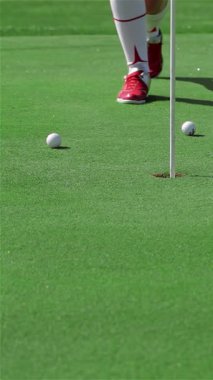 Kararlı genç bir Kafkasyalı kadın, golf topuna sarsılmaz bir hassasiyetle vurmaya hazırlanan canlı zümrüt çimlerin üzerinde zarafetle diz çöker. Sahne, onun şık kırmızı ayakkabıları tarafından vurgulanan hırs ve spor dolu.