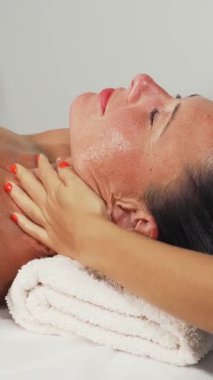 Mutlu, olgun bir kadın, gençleştirici bir kafa ve boyun masajından zevk alır. Huzurlu bir spa ortamındaki saf rahatlamayı yansıtan huzurlu ifadesi. Yumuşak, ortam aydınlatması ve yetenekli terapistin nazik dokunuşu bir dinginlik vahası yaratıyor.