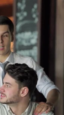 Kahkaha ve tezahüratla dolu hareketli bir barda, keskin gömlekler giymiş iki genç işadamı, televizyonda heyecanlı bir futbol maçını kutlarken bir an olsun neşe paylaşıyorlar. Animasyon ifadeleri ve yoldaşlıkları heyecan saçıyor.