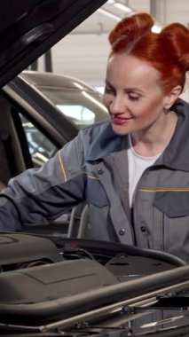 Kızıl saçlı yetenekli ve şık bir bayan tamirci parlak, modern bir garajda şık bir cipin motorunu titizlikle inceliyor. Odaklanmış tavrı ve profesyonel giyimi, uzmanlığını ve kadınların bu konudaki varlıklarını vurguluyor.