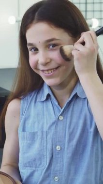 Parlak, şık bir kuaförde makyajını yaparken uzun kahverengi saçlarıyla neşe saçan ışıl ışıl bir kız. Çocukluk masumiyetinin ve yaratıcılığının özünü yakalayan küçük bir güzellik sanatçısı gibi poz verirken neşeli enerjisi yayılıyor.