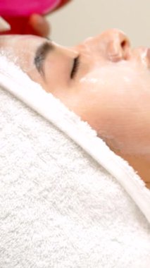 Huzurlu bir Asyalı kız güzellik salonunda, yüzü doğal parıltısını arttıran kremsi bir maskeyle kaplı olarak rahatça uzanıyor. Yetenekli güzellik uzmanı, yaşlanmayı önleyici tedaviyi nazikçe uyguluyor. Kendine bakmanın huzurlu bir vahasını yaratıyor.