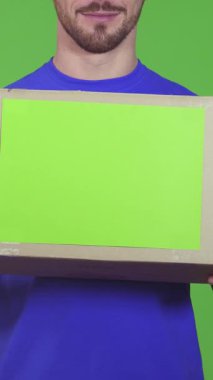 Neşeli, sakallı, parlak mavi gömlekli bir teslimatçı elinde bir karton kutu tutarken heyecanla içeriğini merak ediyor. Bu canlı sahne profesyonelliği ve sıcaklığı yansıtıyor, canlı yeşil bir arka planda geçen