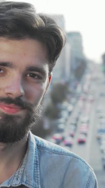 Neşeli, sakallı genç bir adam, hareketli bir şehir manzarası tarafından çerçevelenmiş kameraya gülümserken mutluluk saçıyor. Bu şık hippi, gelişigüzel giyinmiş, genç keşiflerinin ruhunu ve şehir hayatının heyecanını temsil ediyor.