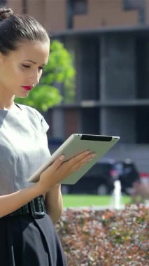 Canlı bir şehir parkında, kendine güvenen genç bir iş kadını tabletiyle meşgul oluyor, profesyonellik ve tarz yayıyor. Onun sıcak gülümsemesi, meslektaşlarının yakınlarda konuştuğu hareketli ve dinamik bir çalışma atmosferini somutlaştıran hareketli sahneyi aydınlatıyor.