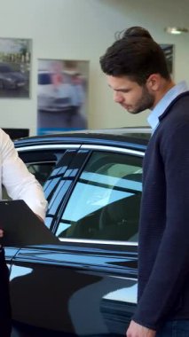Gıcır gıcır beyaz gömlekli kendine güvenen sarışın bir satıcı her ikisi de sıkı bir tokalaşmayla meşgul şık esmer sakallı bir müşteriye panoda ayrıntıları sunuyor. Pırıl pırıl, siyah bir arabanın parlak arka planına kurulmuş bu canlı sahne...
