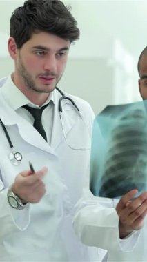 Modern, güneşli bir hastanede, kızıl saçlı ve gözlüklü bir kadın da dahil olmak üzere üç kendine güvenen doktor, sağlıklı akciğerlerin röntgenini dikkatle analiz ediyor. Odaklanmış ifadeleri ve beyaz önlükleri takım çalışmasına ve hasta bakımına bağlılıklarını yansıtıyor.