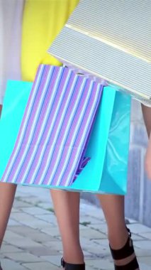 Üç modaya uygun kız, her biri neşeli renklerde canlı alışveriş torbaları taşıyor, şık bir alışveriş bölgesinde gezinirken neşe saçıyorlar. Kahkahaları ve şık kıyafetleri, perakende satışın heyecanını somutlaştıran kaygısız bir arkadaşlık ortamı yaratıyor.