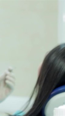 Maske ve eldiven takmış çalışkan genç bir dişçi, parlak ve klinik bir ortamda hastaların dişlerini titizlikle inceliyor. Işıldayan diş aletleri ve odaklı ışıklandırma profesyonellik atmosferi yaratır