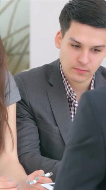 Keskin profesyonel giysiler içinde odaklanmış genç bir çift şık, modern bir ofiste bir iş analistiyle animasyon tartışması yapıyor. Kararlı ifadeleri ve işbirlikçi enerjileri, girişimcilerin sinerjisini vurguluyor