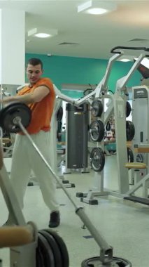 Orta Doğu kökenli kendini adamış genç bir adam canlı bir spor salonunda halter kaldırıyor. Göğsü ve pazıları üzerinde çalışırken odaklanma ve kararlılık yayıyor. Renkli ekipmanlar ve parlak ışıklandırmalarla donatılmış modern spor salonu,