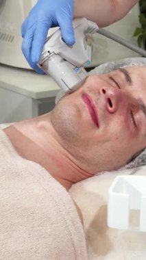 Yakışıklı bir adam lüks bir tedavi yatağında uzanıp şık bir kozmetoloji kliniğinde ultrason terapisinin rahatlatıcı etkilerinin tadını çıkarıyor. Yetenekli güzellik uzmanımız ileri teknolojiyi yüzüne doğru nazikçe süzüp gençlik parıltısını arttırırken...