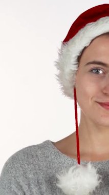 Göz kamaştırıcı kırmızı Noel şapkalı genç bir kadın elleri inanmazlık içinde yanaklarına bastırılmış saf bir şaşkınlık sergiliyor. Bu hoş görüntü, bayram neşesinin özünü yansıtıyor. Ruhu somutlaştıran sıcaklık ve heyecan yayıyor.