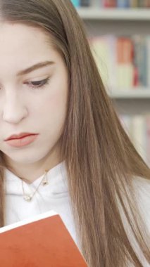 Uzun, ipeksi saçlı düşünceli bir genç kız, parlak raflarla süslenmiş rahat bir kütüphanede turuncu bir kitabı tutarak yukarı bakıyor. Bu sakin sahne, öğrenmenin hazzını ve hayal gücünü besleyen sınırsız merakı güzel bir şekilde özetliyor.