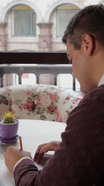 Esmer saçlı genç beyaz bir adam büyüleyici bir kafede kahvenin zengin aromasının tadını çıkarıyor. Not defterine notlar yazmakla çok meşgul. Samimi bir süveter giyerek, açık sayfalara düşünceli bir şekilde sarı bir kalem yerleştirir.