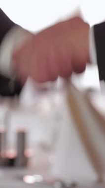 Yumuşak ışıklandırma ve zarif dekor ile süslenmiş şık bir restoranda, iki iyi giyimli iş adamı sıkı bir tokalaşma içinde, umut verici bir ortaklığı sağlamlaştırıyorlar. Atmosfer işbirliği ve karşılıklı saygı yayıyor.