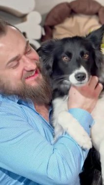 Şık sakallı neşeli bir adam neşeli köpeğini kucaklıyor. Her ikisi de renkli oyuncaklar ve hediyelerle dolu canlı bir evcil hayvan dükkanında mutluluk saçıyor. Tapılası köpek, parlak siyah beyaz kürkü ve sallanan kuyruğuyla sıcak atmosferi güçlendirir.