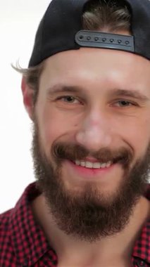 Havalı bir şapka ve kareli gömlek giyen şık, genç sakallı bir adam yumuşak beyaz bir arka plana sıcak bir gülümseme sergiliyor. Hipster havası ve rahat tavırları modern zarafeti yansıtıyor. Bu da onu çağdaş modanın büyüleyici bir figürü yapıyor.