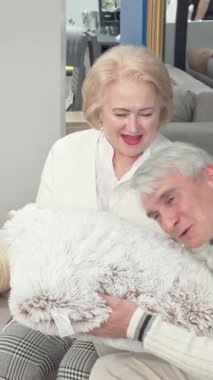 Zevkli, yaşlı bir çift şık bir mobilya mağazasında lüks yastıklar seçiyor, sıcaklık ve sevgi saçıyor. Neşeli kadın, parlak kırmızı dudaklarıyla, kocasıyla bir kahkaha paylaşıyor, iç açıcı bir sahne yaratıyor.