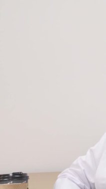 Deniz mavisi aksanlı, gevrek beyaz bir palto giymiş dingin, olgun bir kadın doktor, düşünceli bir şekilde uzaklığa bakarken sıcak bir fincan kahvenin tadını çıkarıyor. Bu sakin sahne, kendine bakmanın ve yansımanın önemini güzel bir şekilde ortaya koyuyor.