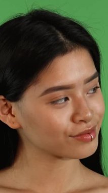 Çekici genç bir Asyalı kadın zarif bir şekilde kenarlara bakar, uzun, ipeksi koyu saçları zarif bir şekilde akarken, yüzünü aydınlatan büyüleyici bir gülümseme ortaya çıkar. Parlak yeşil bir krom anahtar arkaplan ile ayarlandığında, bu an yayılır