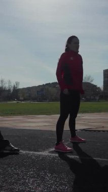 Enerjik atletizm kıyafetleri içinde iki enerjik genç kız güneşli bir pistte dinamik bacak ısıtma egzersizleri yapıyorlar. Önlerindeki yarışa hazırlanırken somut kararlılıklarını gösteriyorlar. Sahne heyecan ve odaklanma yayar, özünü yakalar.