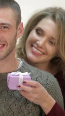 Hoş süveter giyen neşeli bir kadın, her ikisi de Noel Baba şapkasıyla süslenmiş gülümseyen erkek arkadaşına eğlenceli bir mor hediye sunar. Bu nefis sahne sıcaklığı ve sevgiyi yansıtıyor, Noel neşesinin özünü yakalıyor ve neşeli bir şekilde paylaşıyorlar.