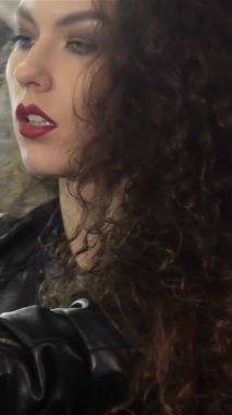 Çarpıcı bir bayan motorcu motosiklet koltuğuna yaslanıyor, kendine güven ve tarz yayıyor. Lezzetli kıvırcık saçları ve neşeli kafasıyla, bu parlak siyah deri ceketli beyaz kadın macera ruhunu somutlaştırıyor.