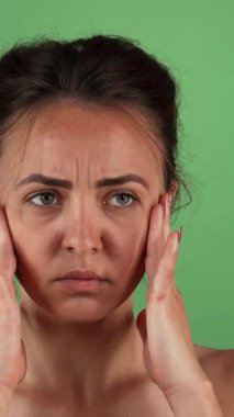 Kaşları çatık ve endişeli bir ifadeyle baş döndürücü genç bir kadın şakaklarını parlak yeşil renkli bir arka plana nazikçe sürtüyor. Bu çarpıcı görüntü anksiyete ve stresin ağırlığını güçlü bir şekilde yakalıyor ve izleyicileri kendisiyle bağlantı kurmaya çağırıyor.